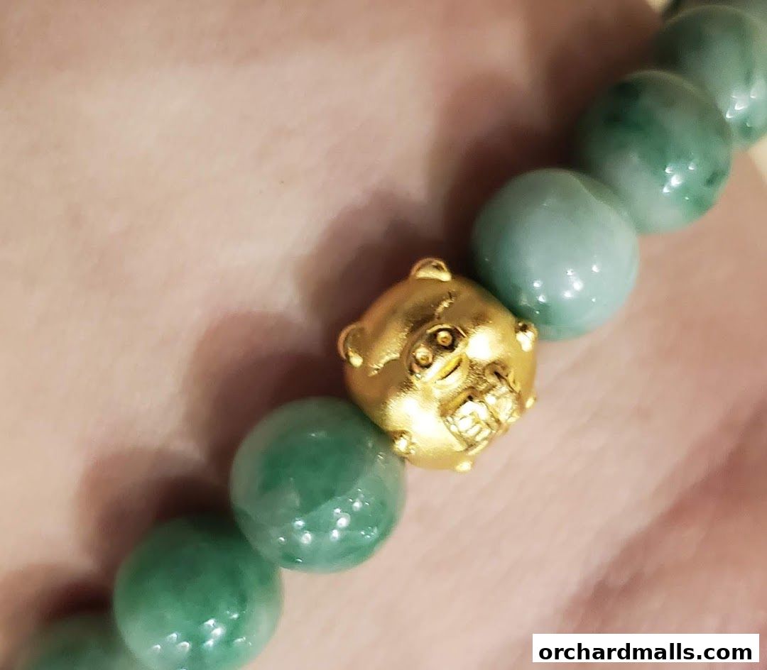 A close-up of a bracelet featuring green jade beads and a gold charm.
