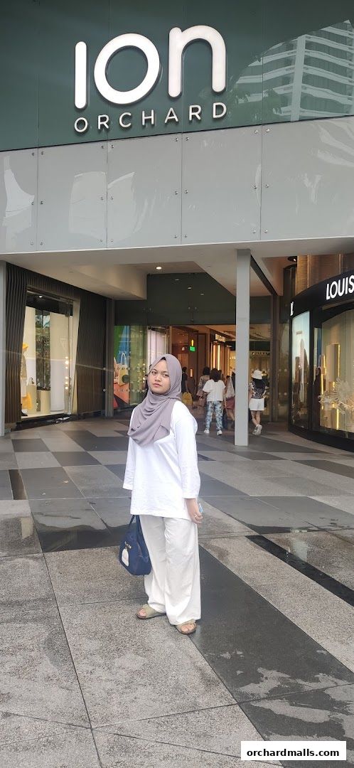 A woman stands in front of the ION Orchard mall entrance, with shops visible inside.