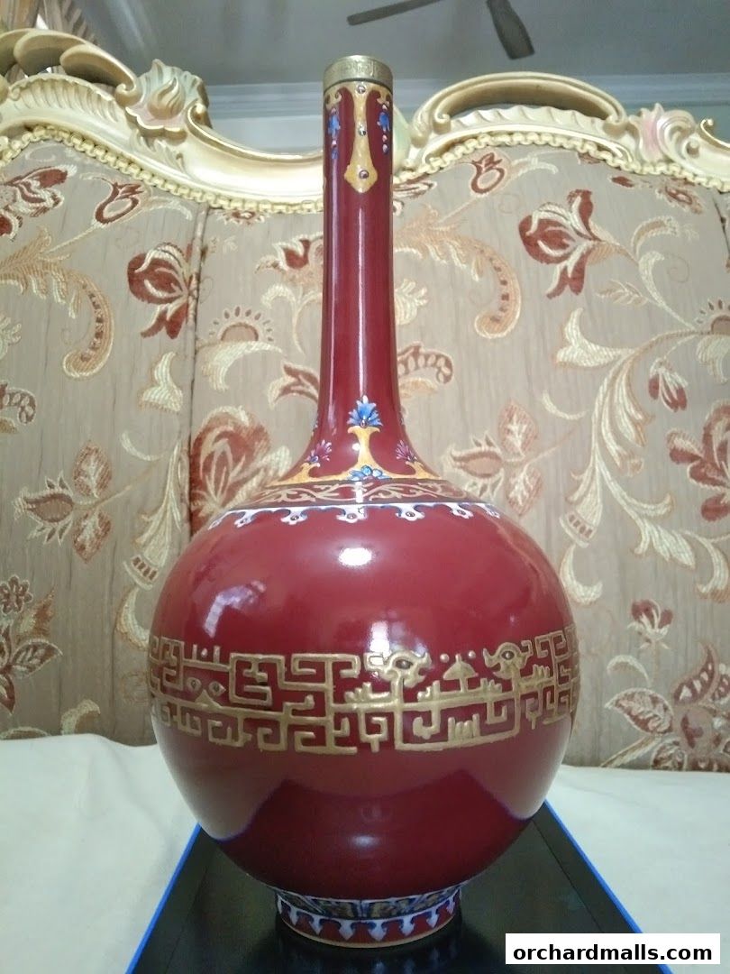 A close-up of a decorative red vase with intricate gold patterns and blue accents.
