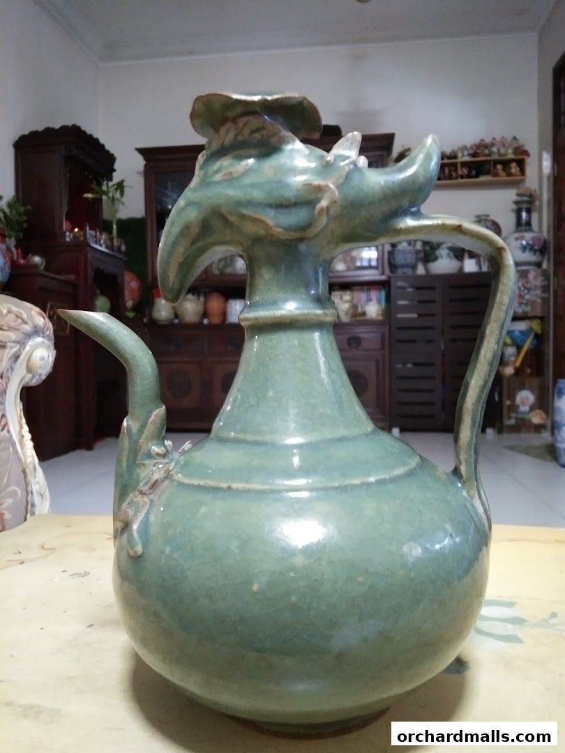 A close-up of an antique celadon-glazed ceramic ewer with dragon-shaped spout and handle.