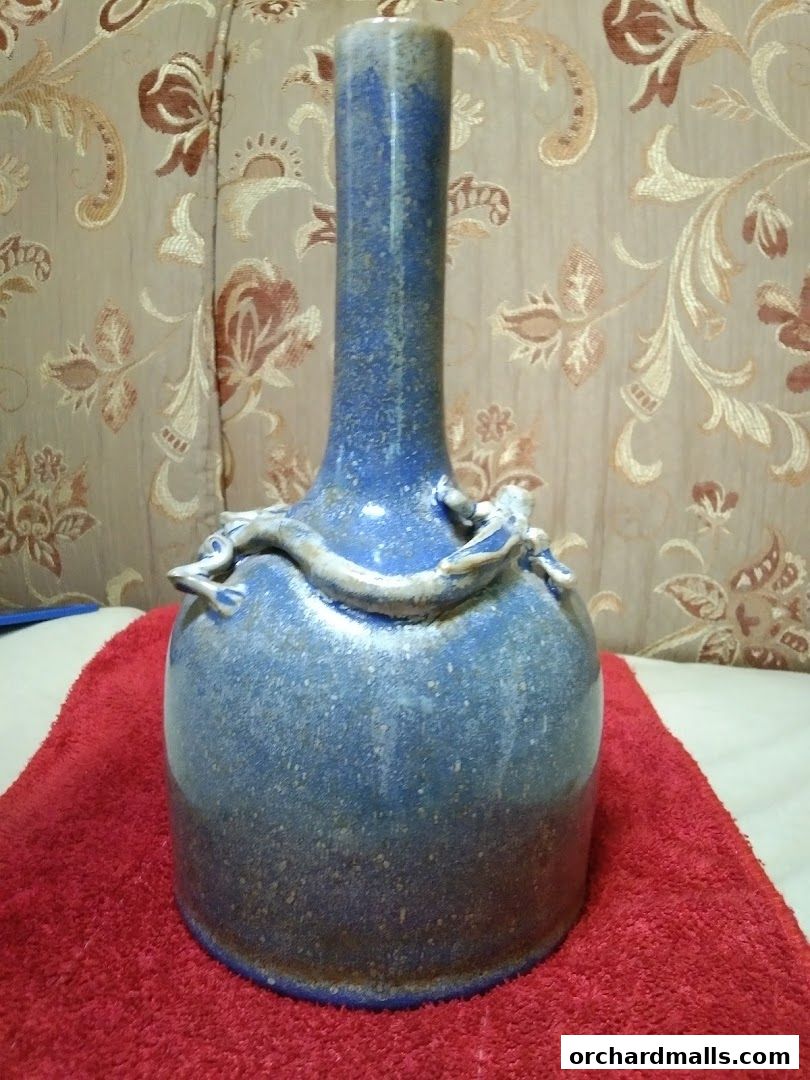 A blue ceramic vase with dragon embellishments sits on a red cloth.