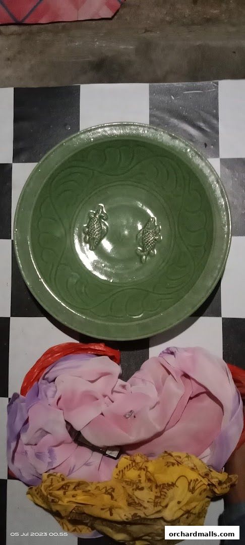 A green ceramic bowl with fish motifs sits on a checkered surface with fabric.