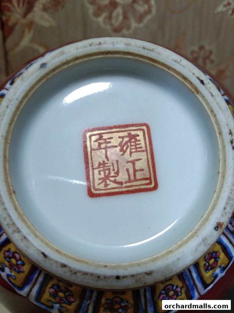 Close-up of a red ceramic vase base with a red stamp and decorative pattern.