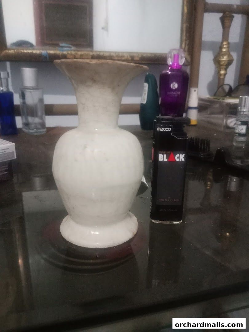 A white marble vase sits on a reflective surface next to a black lighter.