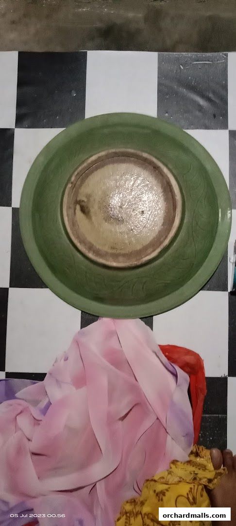 A green ceramic bowl is placed on a black and white checkered floor with fabric draped nearby.