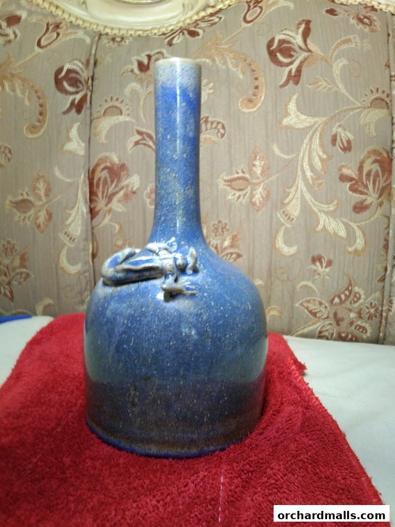 A blue ceramic vase with intricate detailing sits on a red cloth.