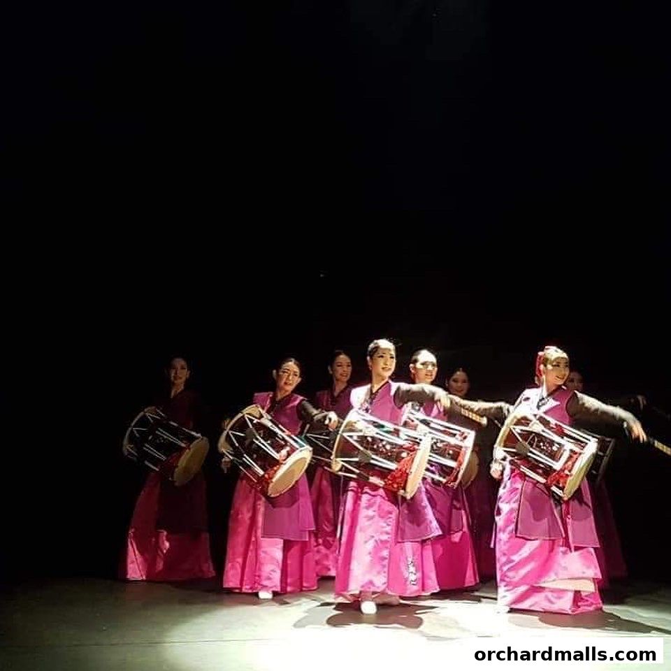 Performers in pink traditional outfits play drums on a dark stage.
