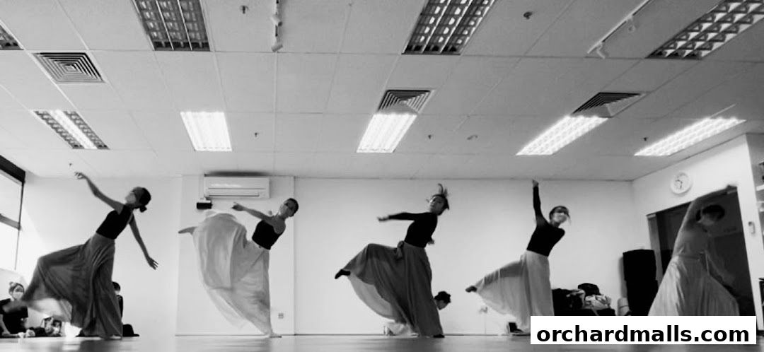 Dancers in flowing skirts practice in a studio with bright overhead lighting.