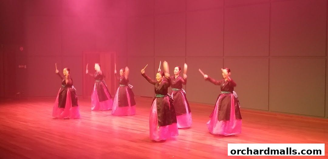 Performers in traditional attire dance on a stage with red lighting.