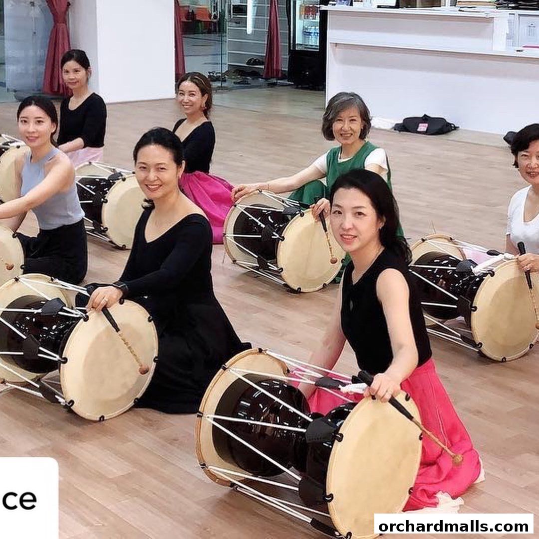 A group of women in traditional attire practice drumming in a studio.