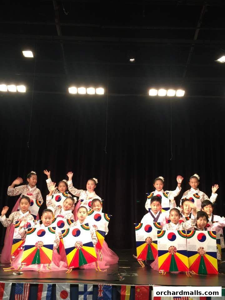 Children in traditional Korean attire perform on stage with colorful props.