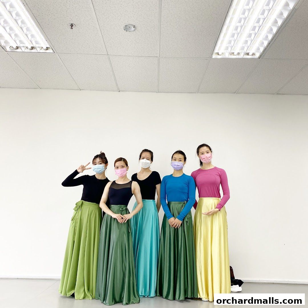 Five dancers in colorful skirts and masks pose in a studio.