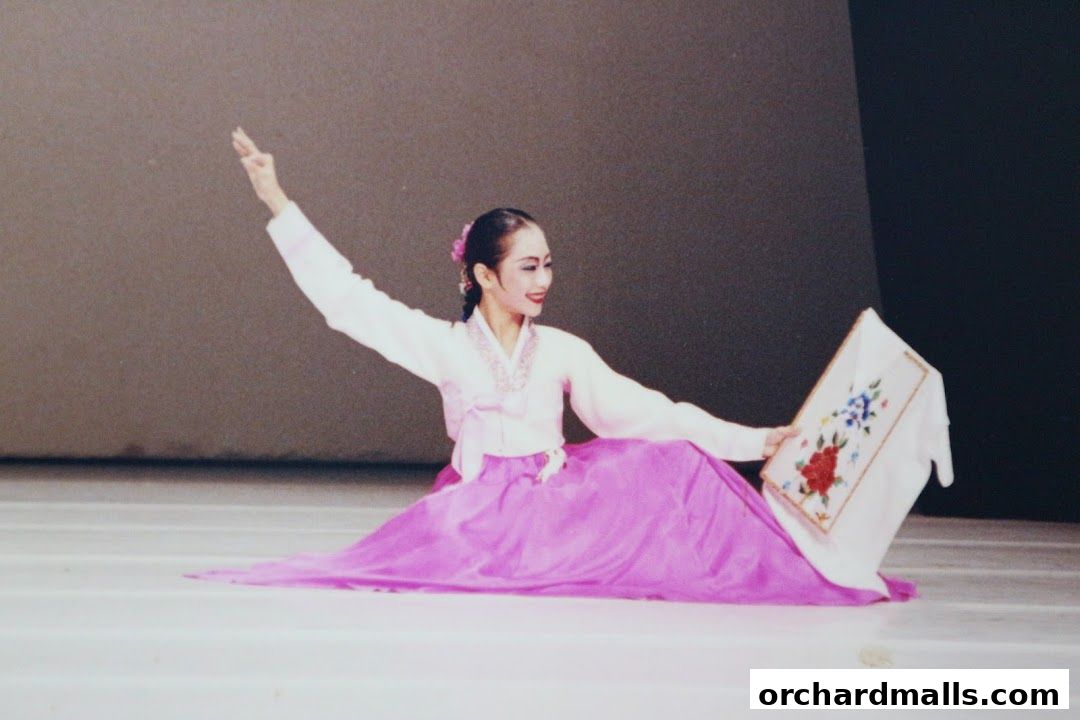A woman in traditional Korean attire performs a graceful dance with a floral embroidered frame.
