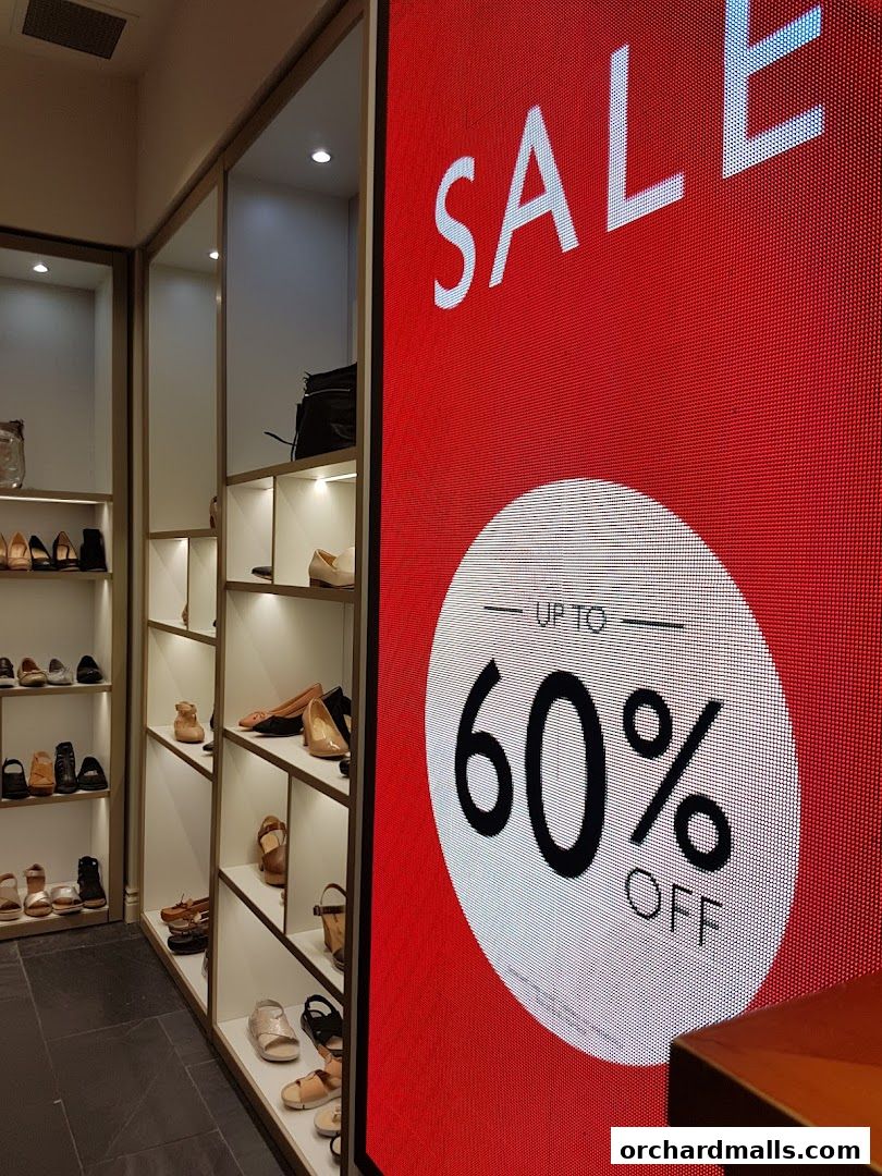 A shoe store interior with shelves displaying various footwear and a large digital sale sign.