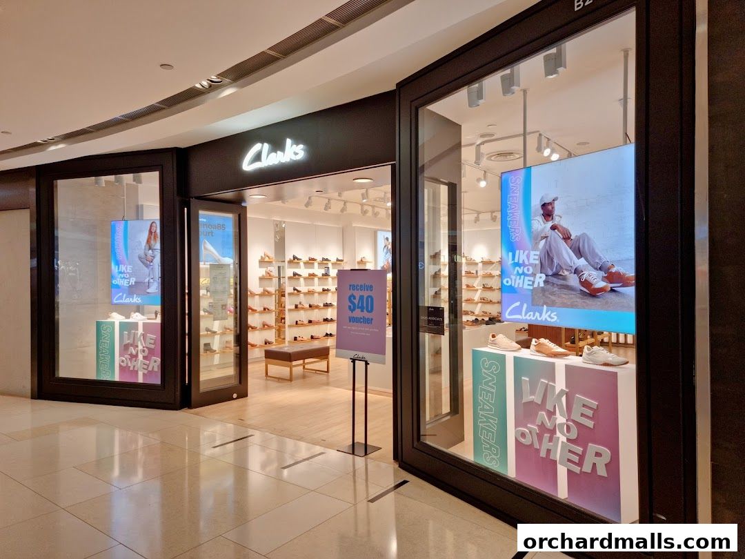 The entrance of a Clarks shoe store with displays of sneakers and a voucher offer.