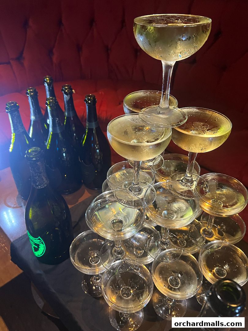 A champagne tower with bottles in the background, set against a red velvet couch.