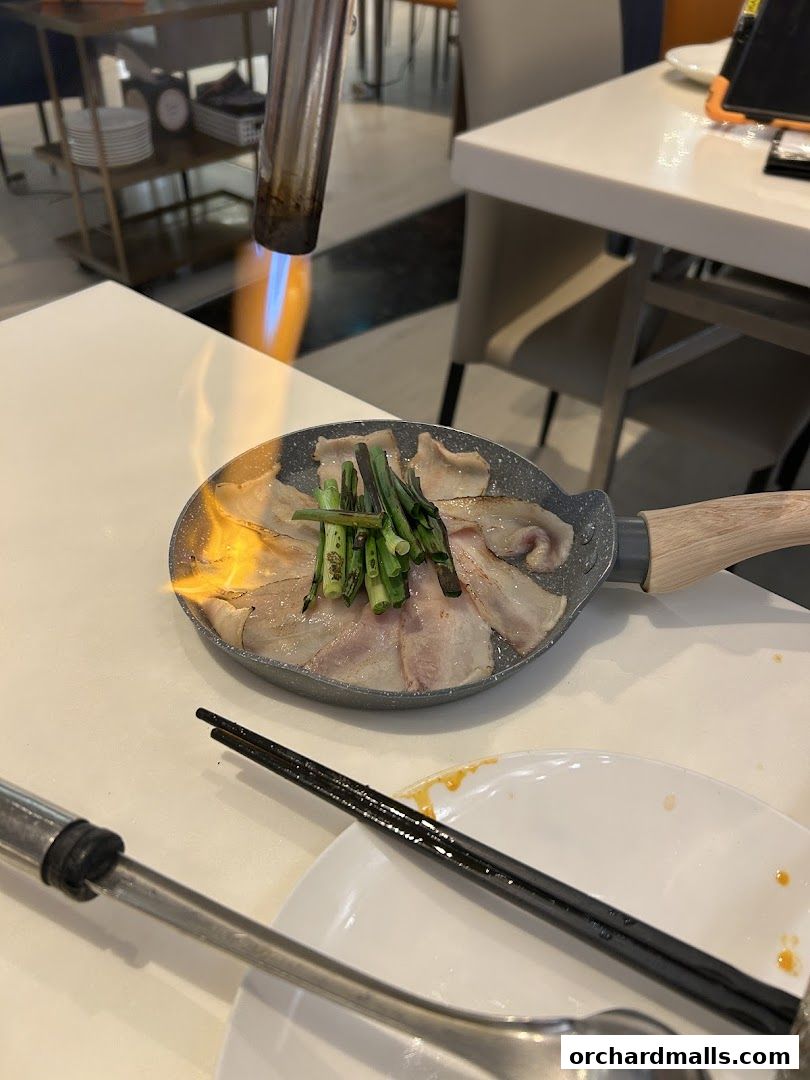A chef is searing meat and vegetables in a pan with a blowtorch.