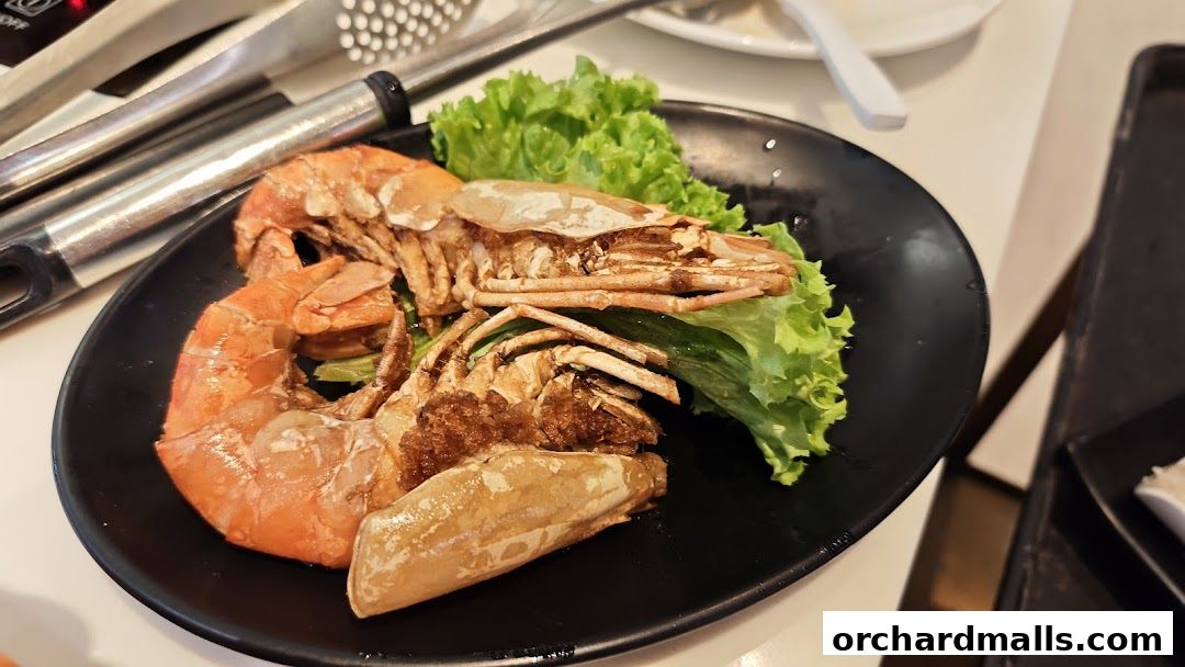 A plate of large, cooked prawns served with lettuce and tongs in the background.