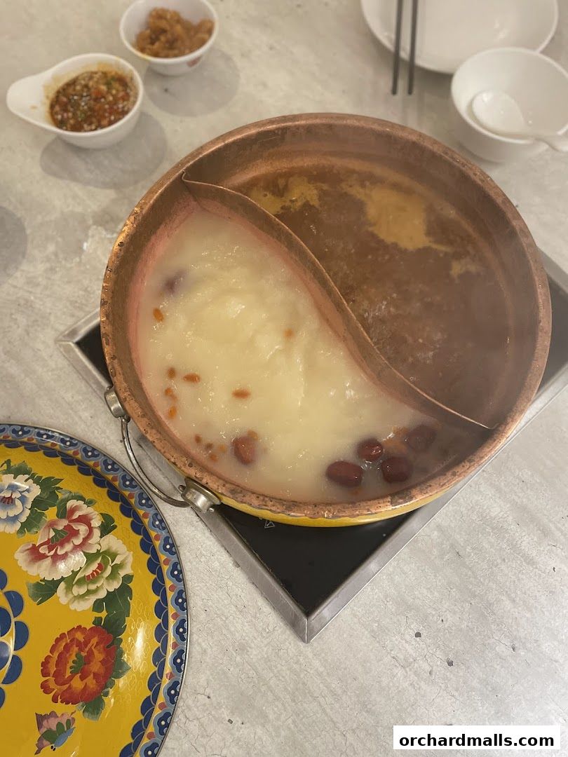 A steaming hot pot with two distinct broths, served with dipping sauces and a decorative lid.