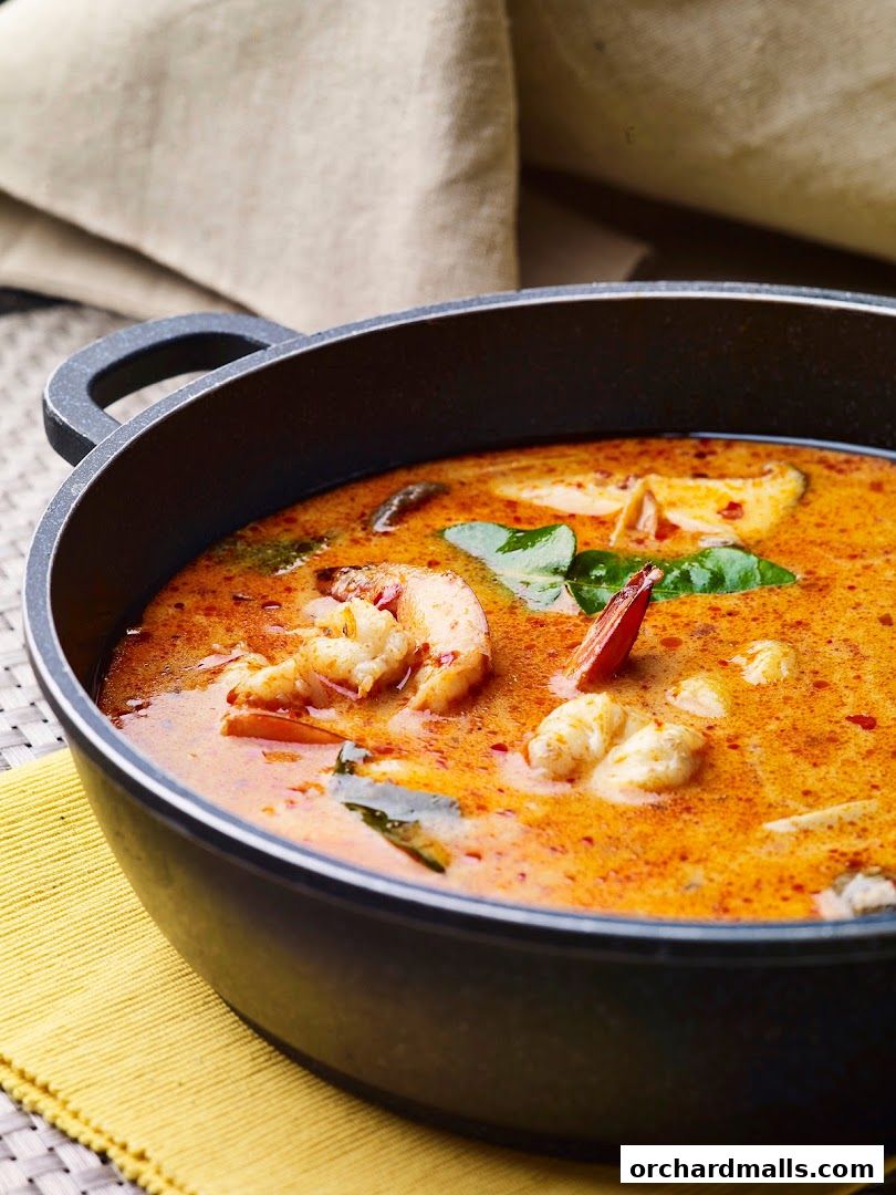 A close-up of a steaming bowl of Tom Yum soup with shrimp and herbs.