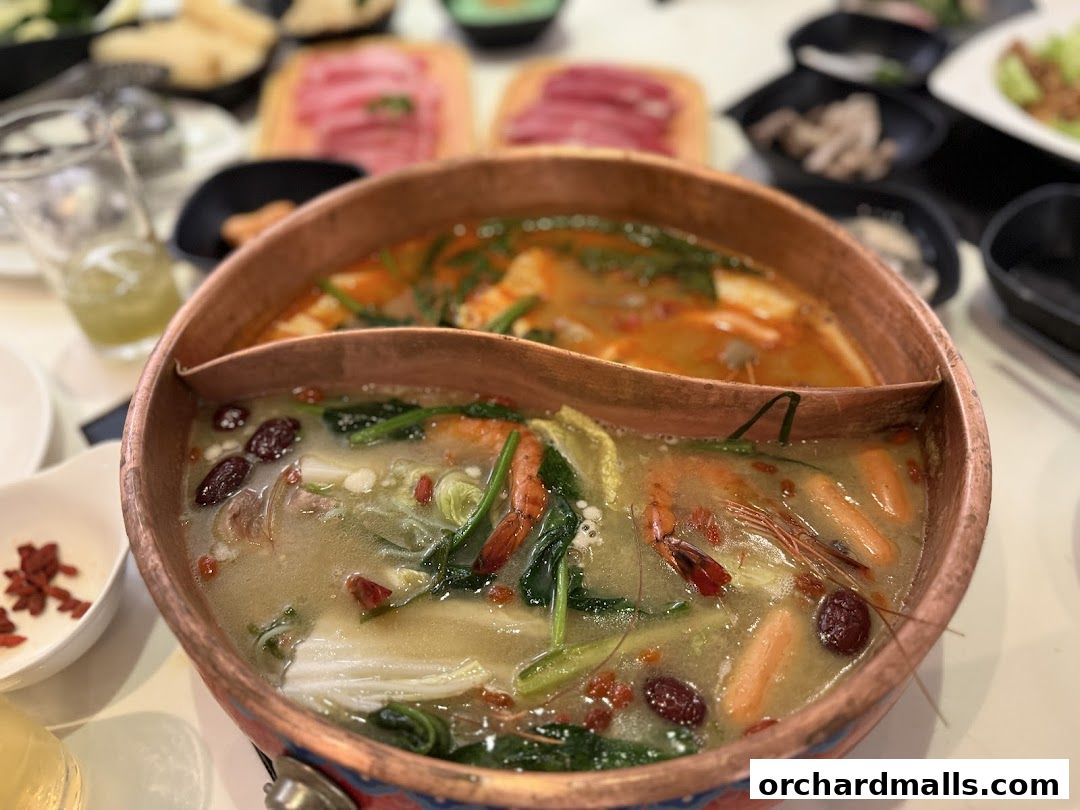 A close-up of a split hot pot with various ingredients like shrimp, vegetables, and goji berries.
