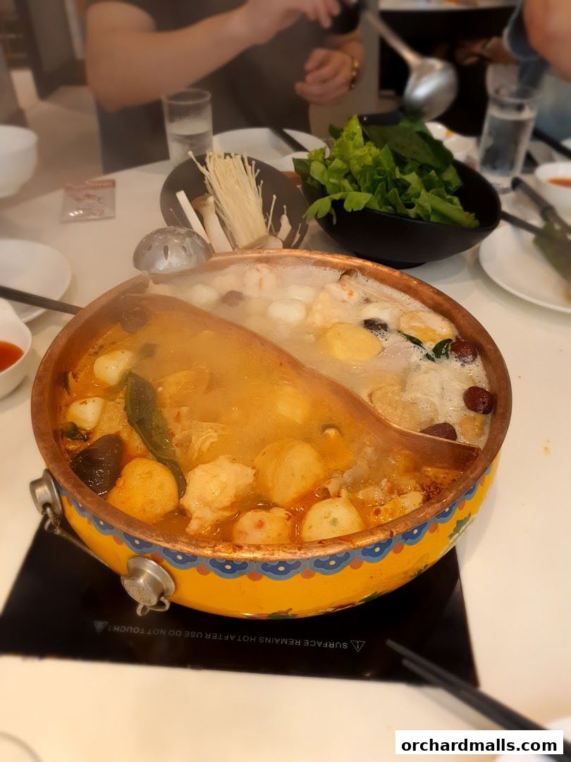 A steaming hot pot with various ingredients and fresh vegetables on a table.