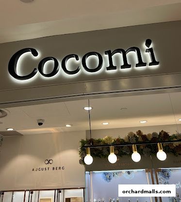 The illuminated Cocomi store sign above a display of watches and floral decor.