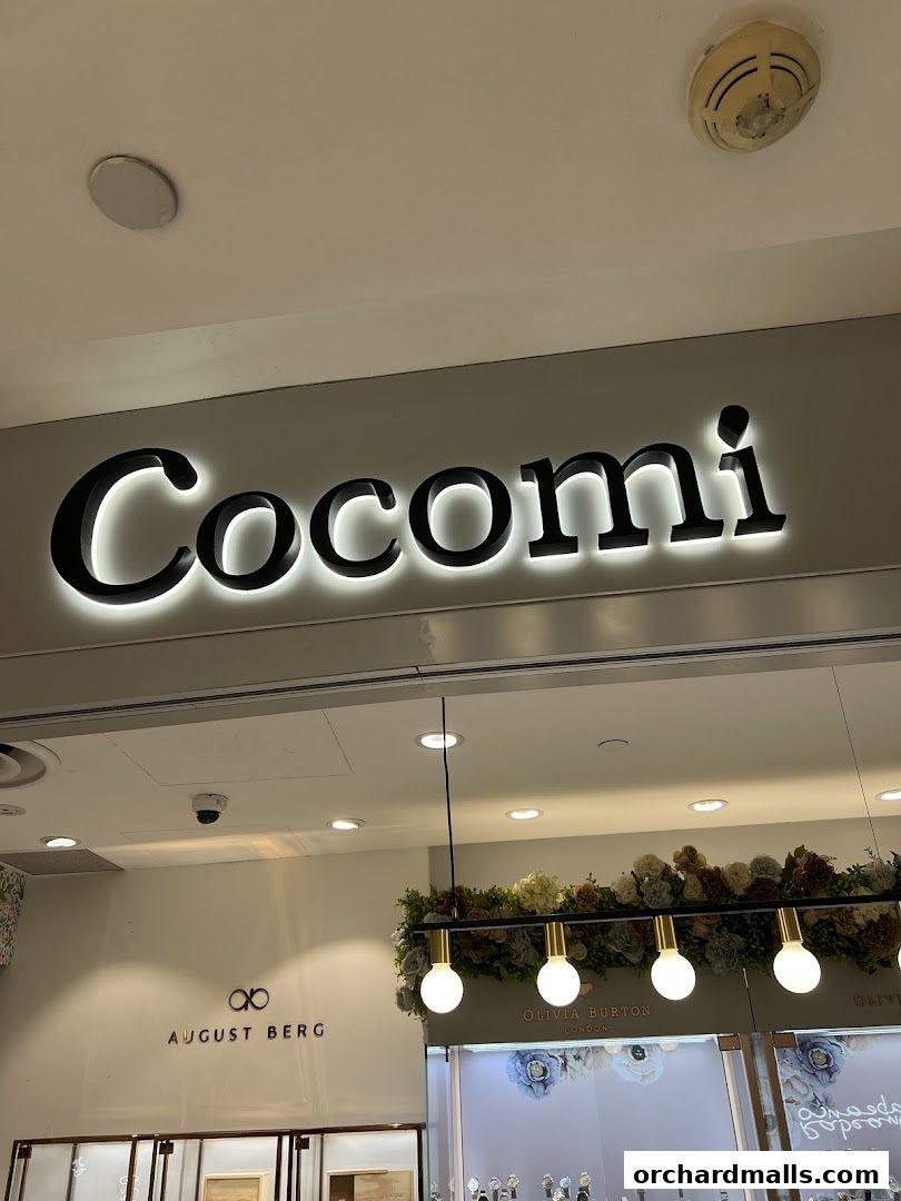The illuminated Cocomi store sign above a display of watches and floral decorations.