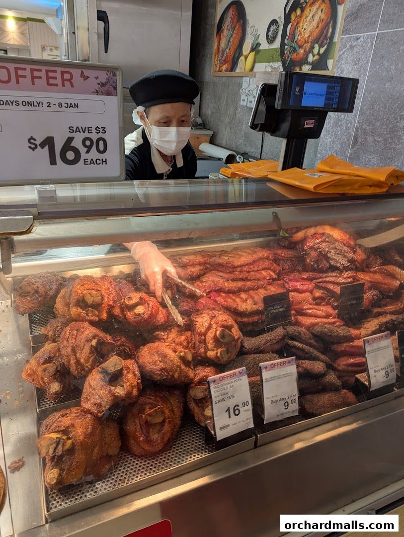 A butcher displays a variety of roasted meats, including pork knuckles, at Cold Storage Takashimaya.