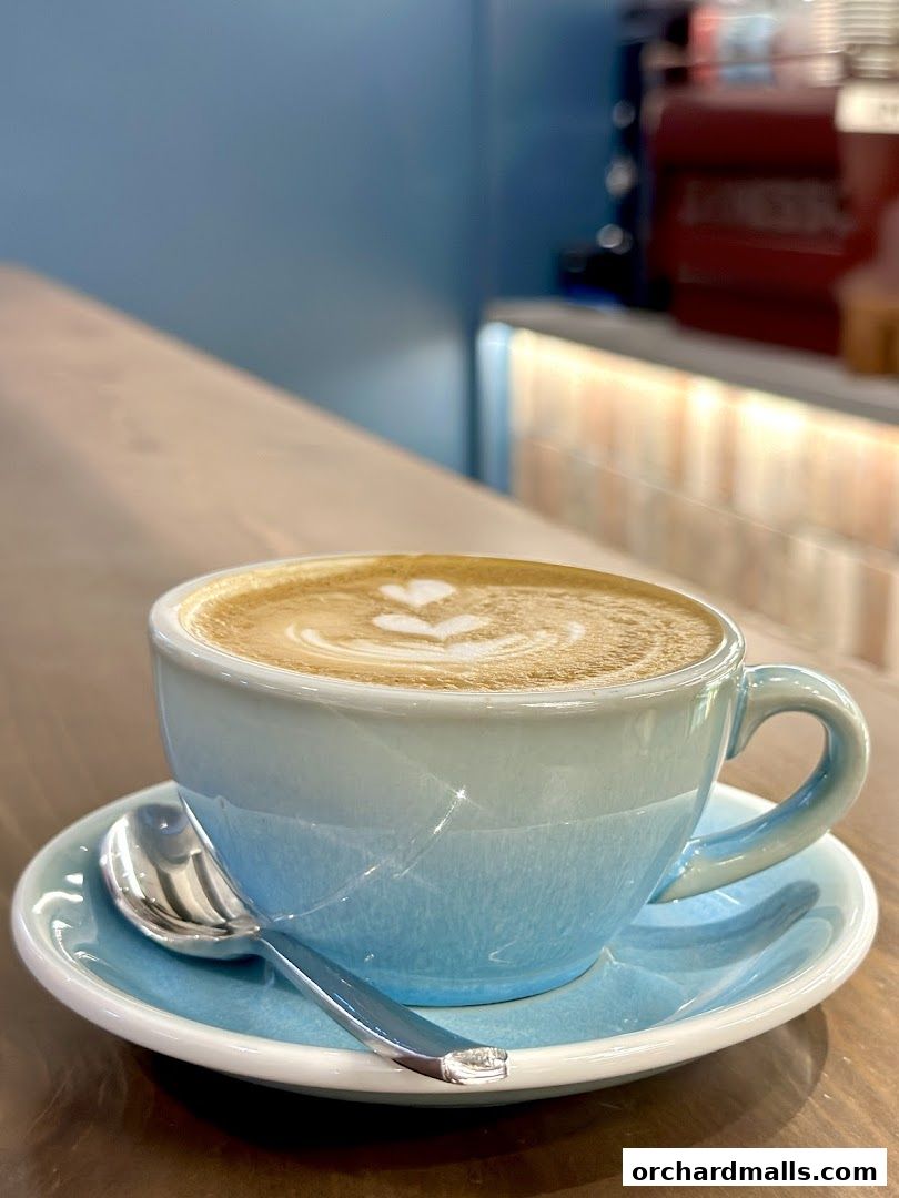 A close-up of a latte with art in a blue gradient cup on a saucer with a spoon.