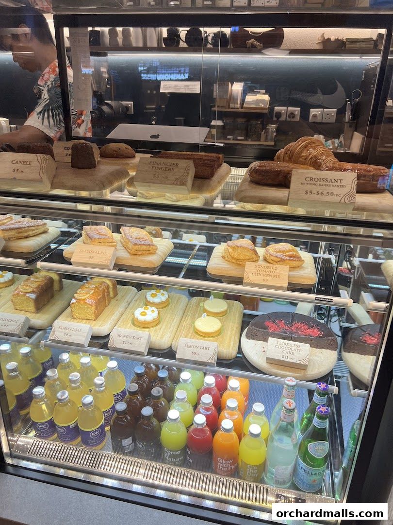 A display case filled with various pastries, cakes, and bottled drinks at Common Man Coffee Roasters.