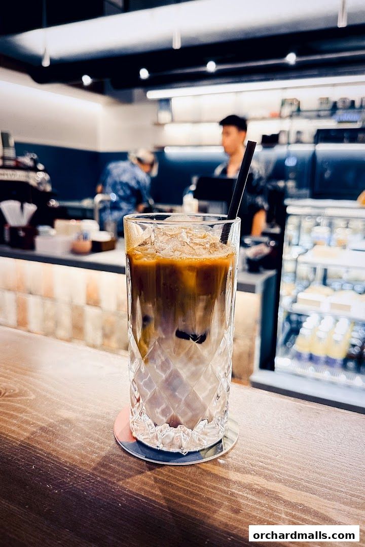 A tall glass of iced coffee with milk and espresso on a wooden counter.