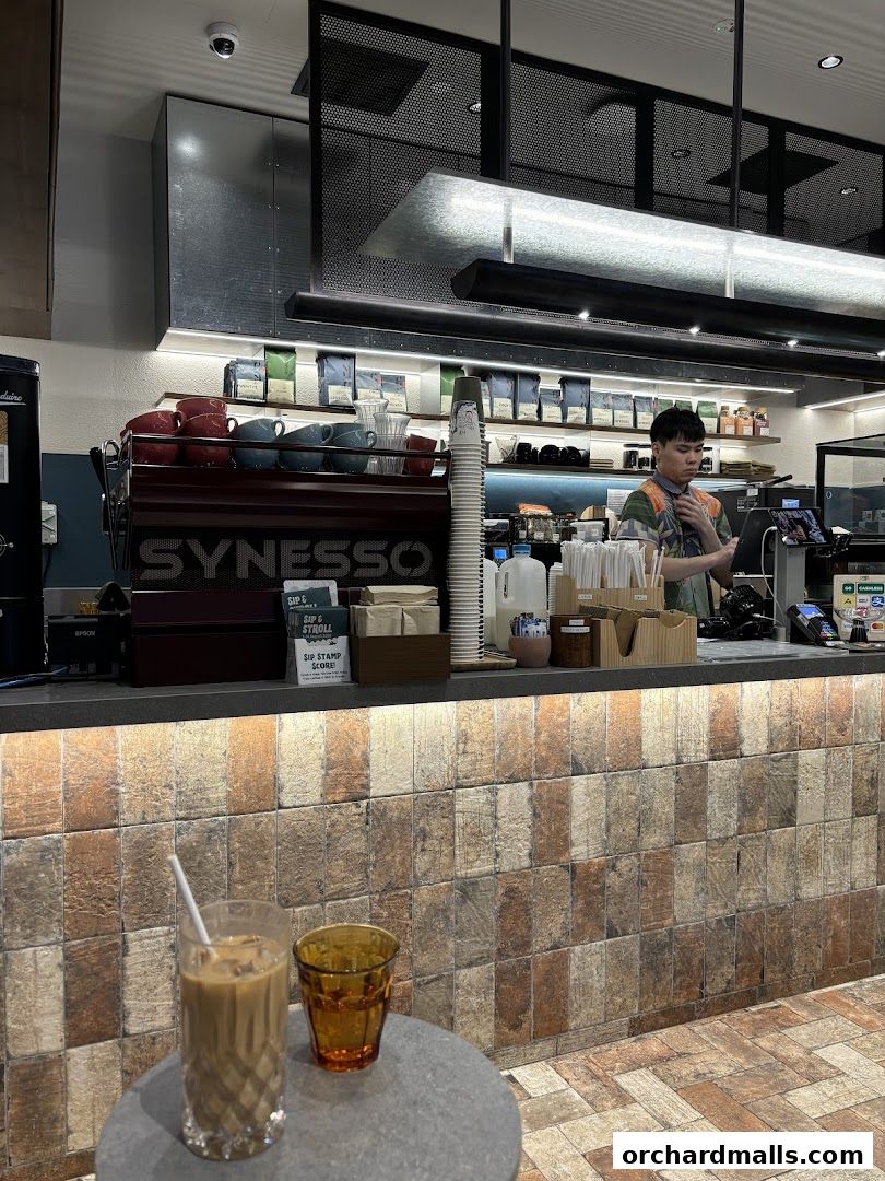 A barista works behind a counter at Common Man Coffee Roasters with coffee cups and bags on shelves.