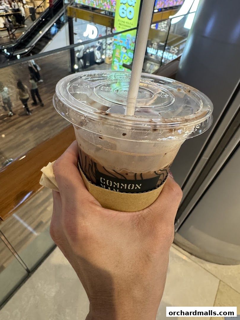 A hand holds a takeaway coffee cup from Common Man Coffee Roasters.
