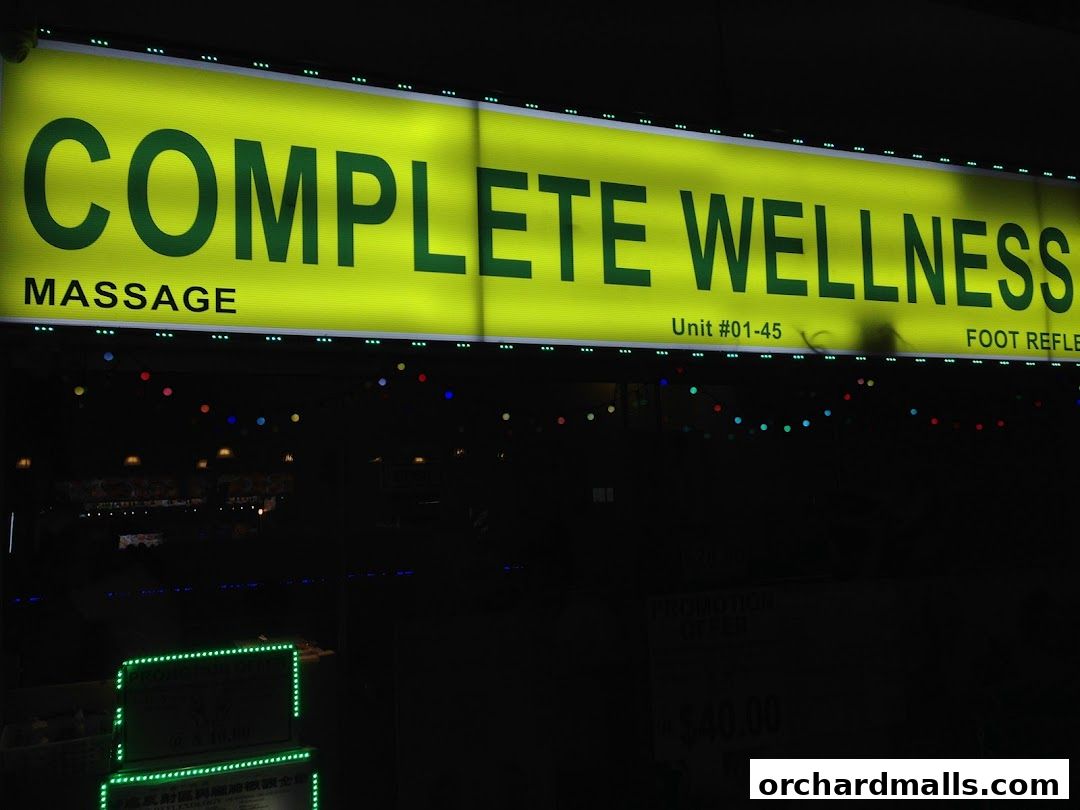 A brightly lit sign for 'Complete Wellness' massage and foot reflexology services.