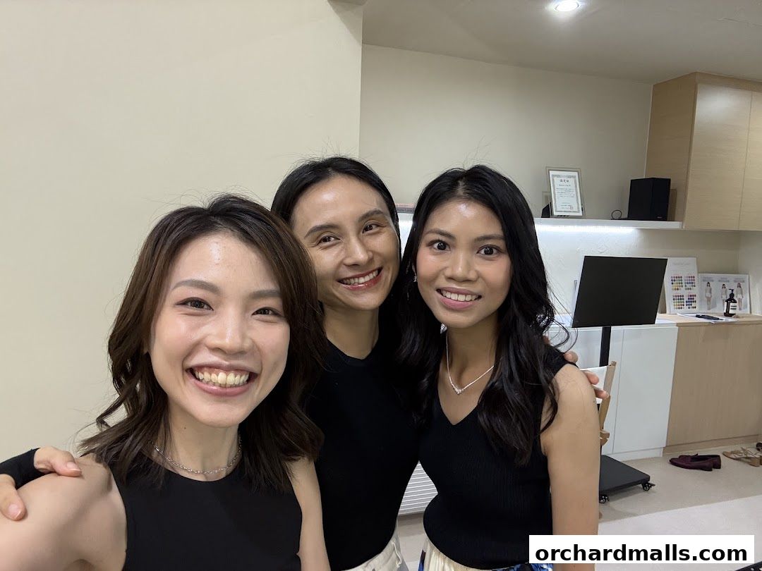Three smiling women posing for a selfie in a bright, modern salon.