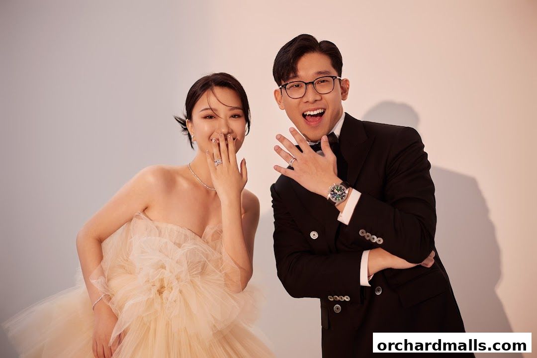 A smiling couple, dressed formally, showing off their rings and a watch.