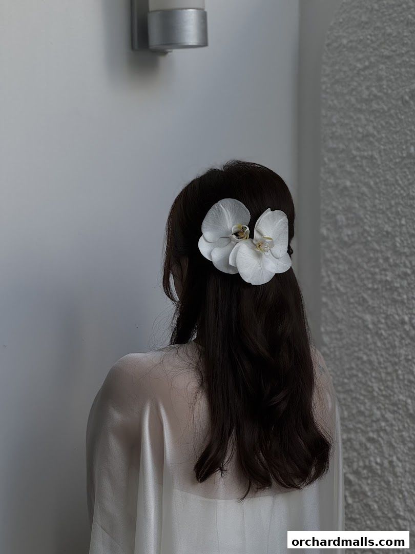 A person with dark hair adorned with a white orchid, styled for a makeover.