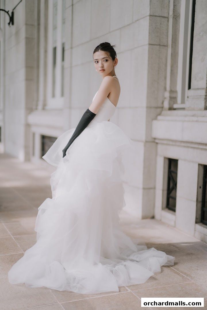 A woman in a white gown and black gloves poses elegantly outdoors.