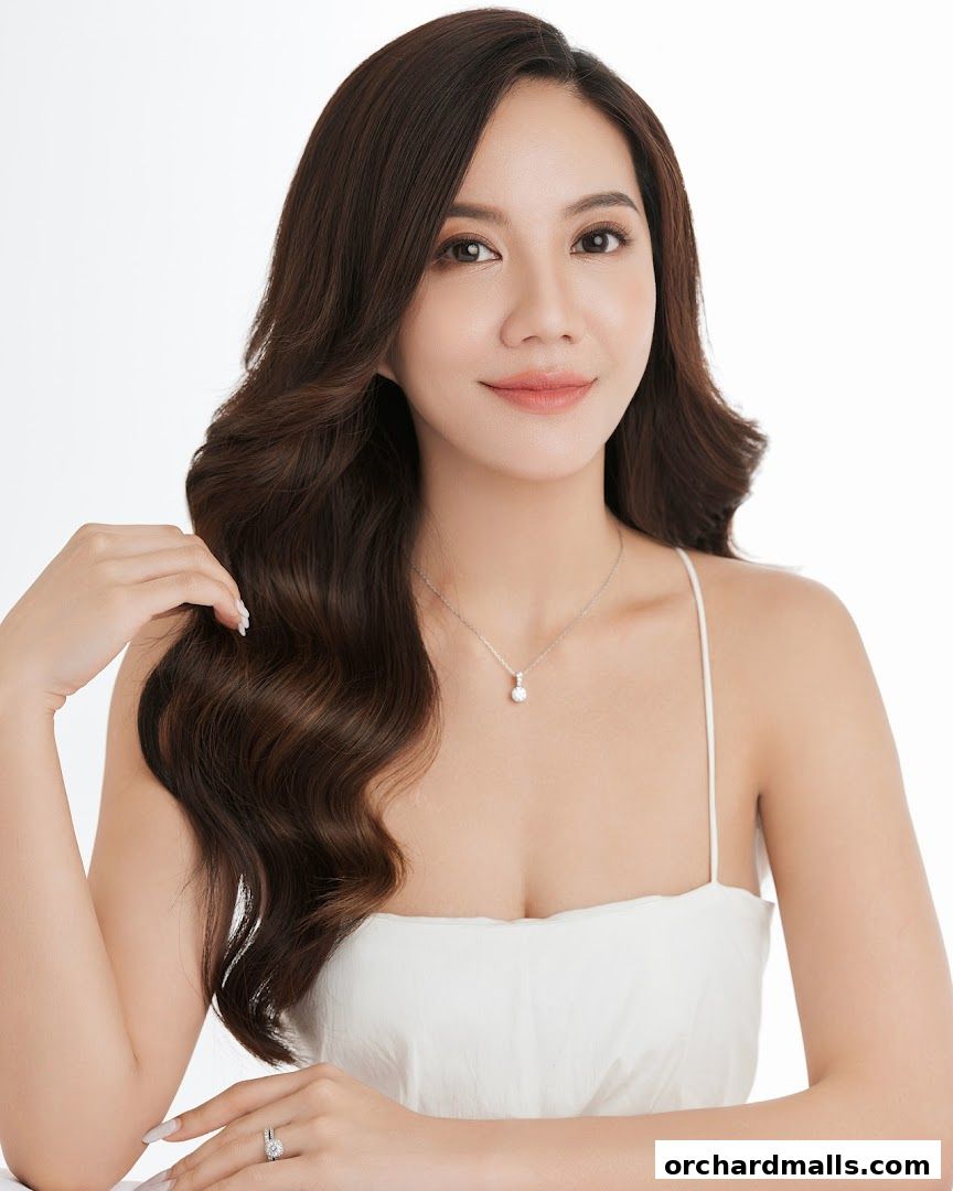 A woman with long, wavy brown hair and makeup, wearing a white dress and jewelry.