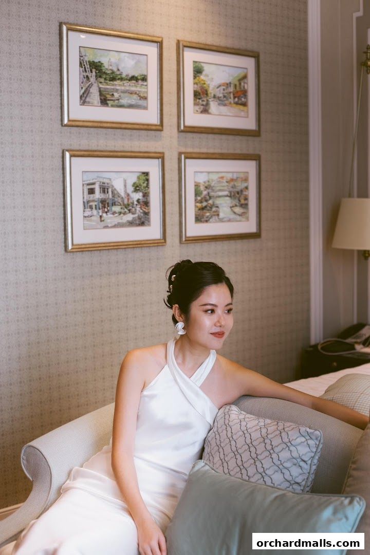 A woman in a white dress sits on a sofa, with framed artwork on the wall.