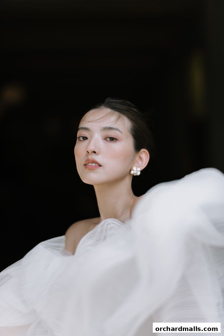 A woman with elegant makeup and pearl earrings, draped in white fabric.