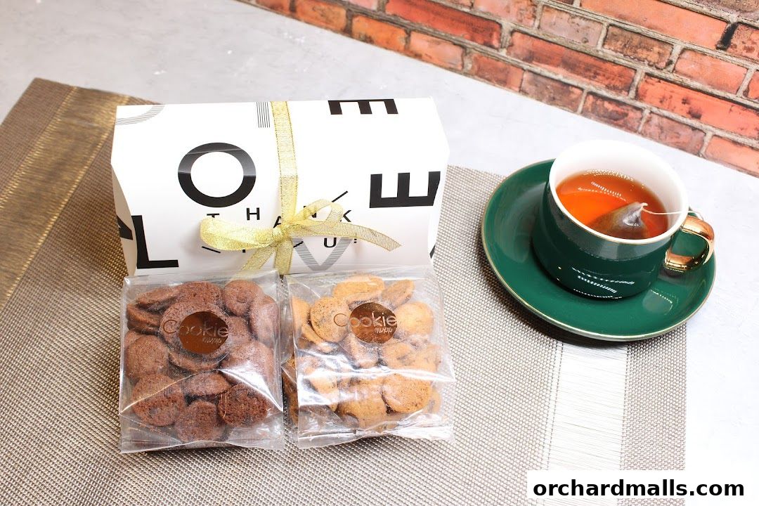 A gift box with two bags of cookies and a cup of tea.