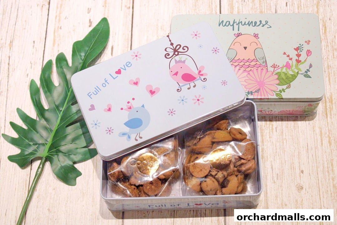 Two decorative cookie tins, one open, filled with cookies, next to a green leaf.
