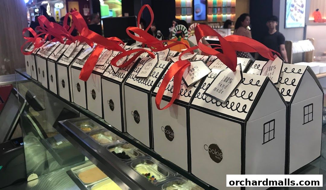 A display of house-shaped cookie boxes with red ribbons and '100% Hand Made' tags.