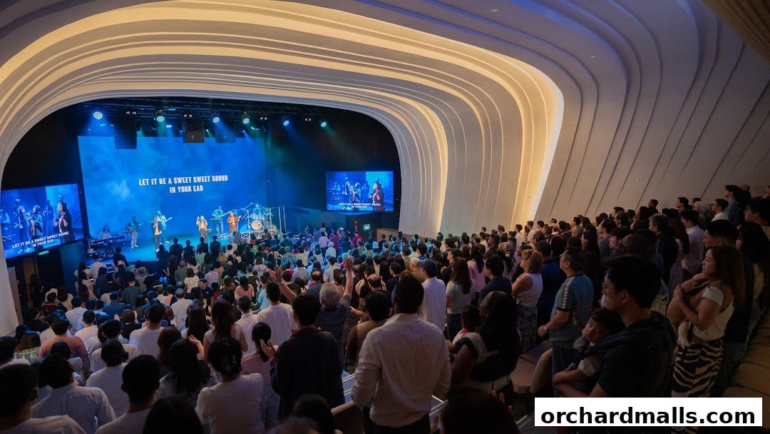A large congregation watches a band perform on stage in a modern church auditorium.
