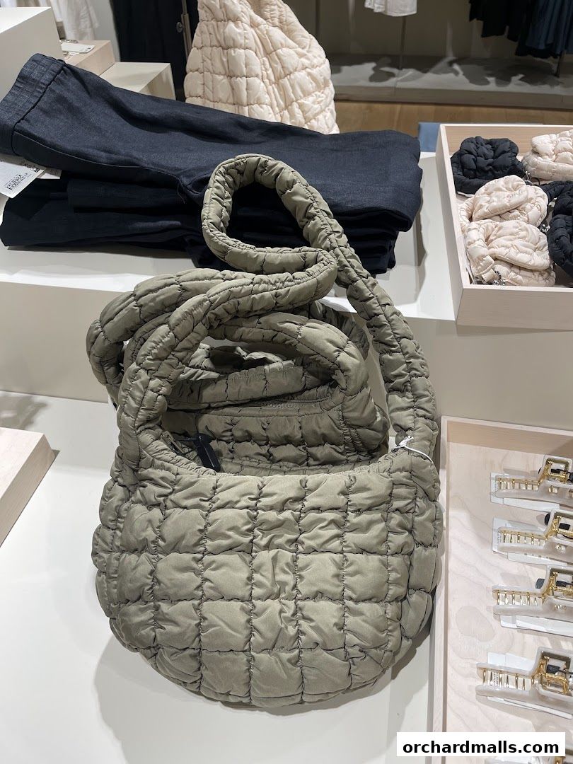 A quilted handbag is displayed alongside folded dark trousers and other accessories in a retail store.