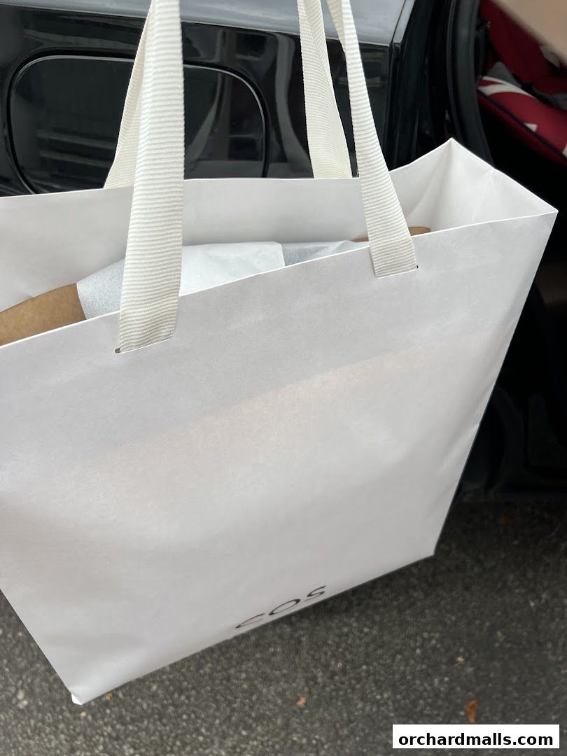 A white shopping bag with the COS logo and white handles, containing items.
