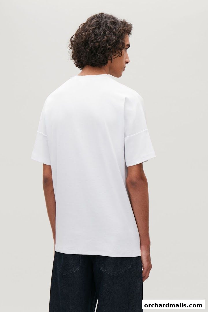 A man models a white COS t-shirt and dark denim jeans against a plain background.