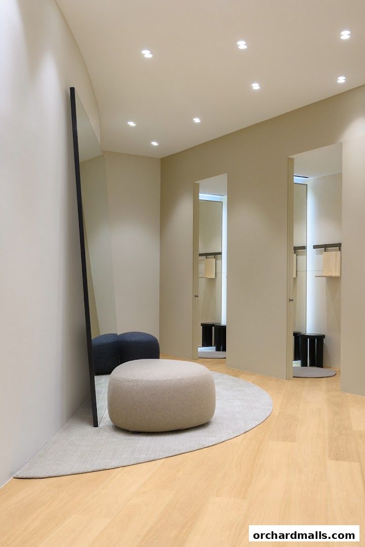 A modern fitting room with a large mirror, comfortable seating, and two open doorways.